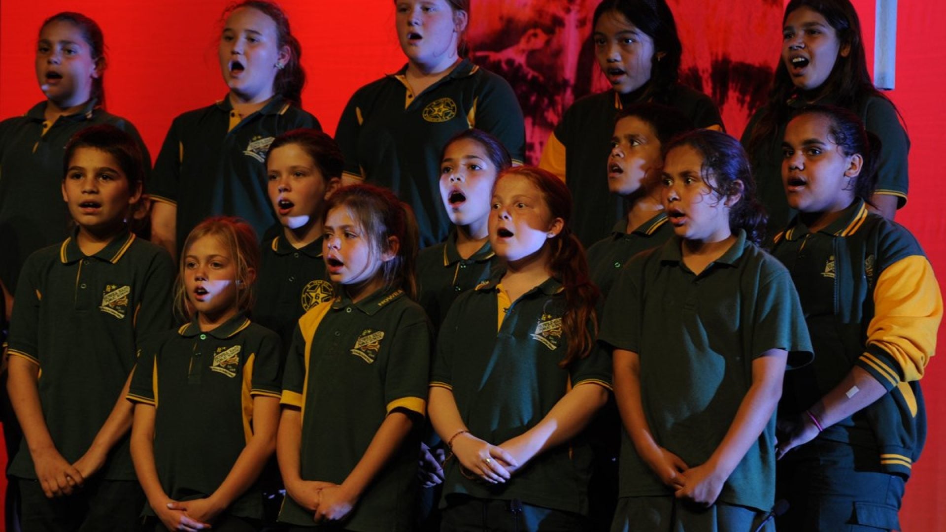 15 young people standing together in green school uniforms , singing