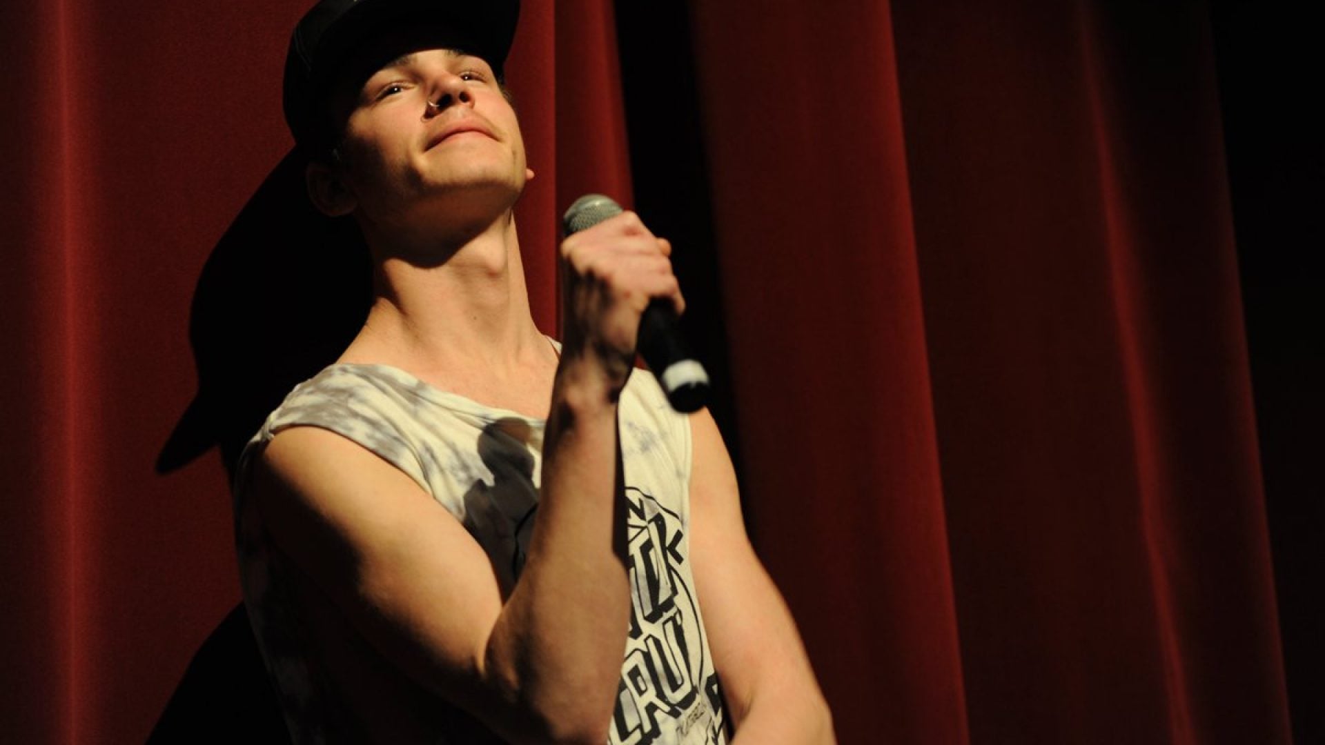 Person in a singlet and a cap holds a microphone up to their mouth