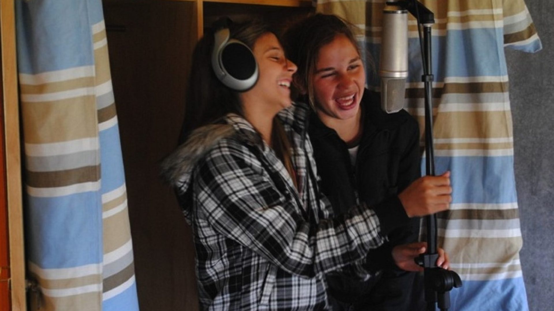 2 teenagers laughing into a microphone. 1 is wearing headphones