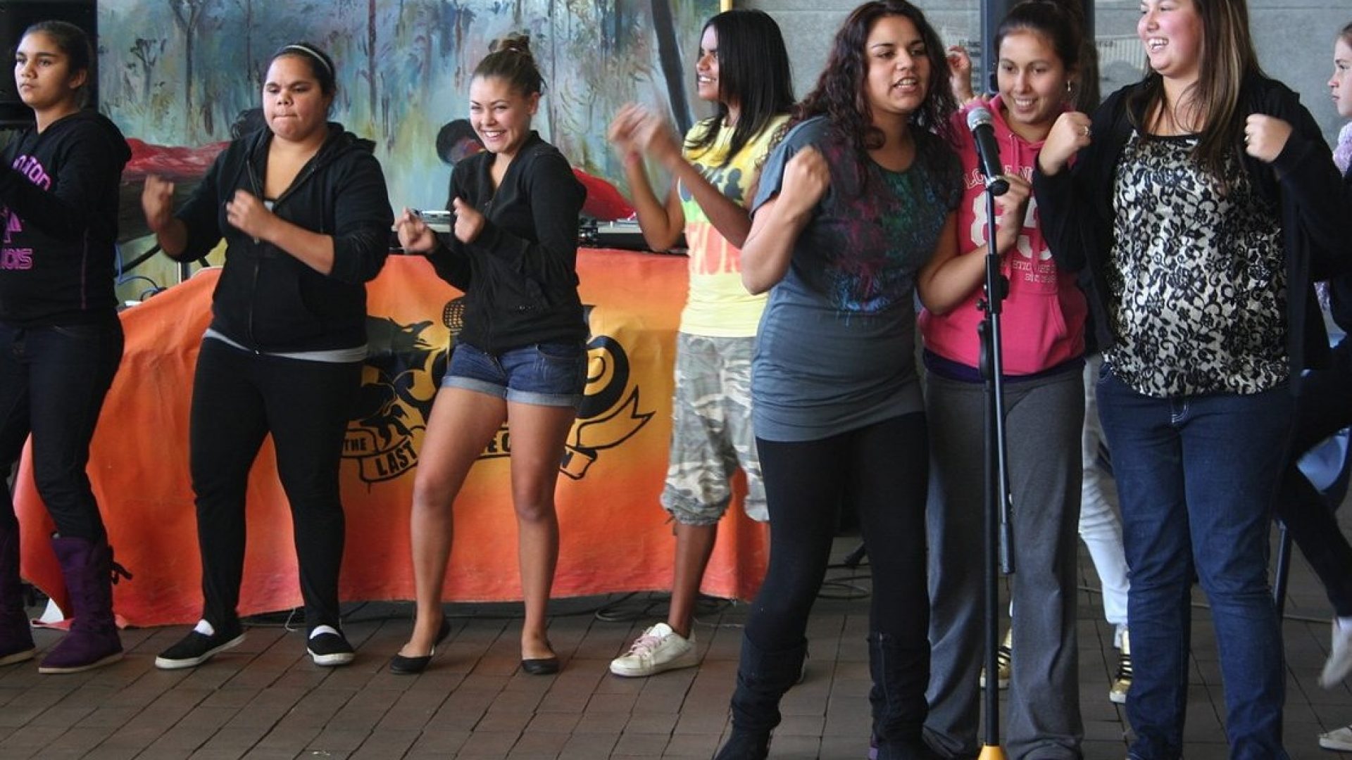 8 young teenagers dancing and singing into a microphone