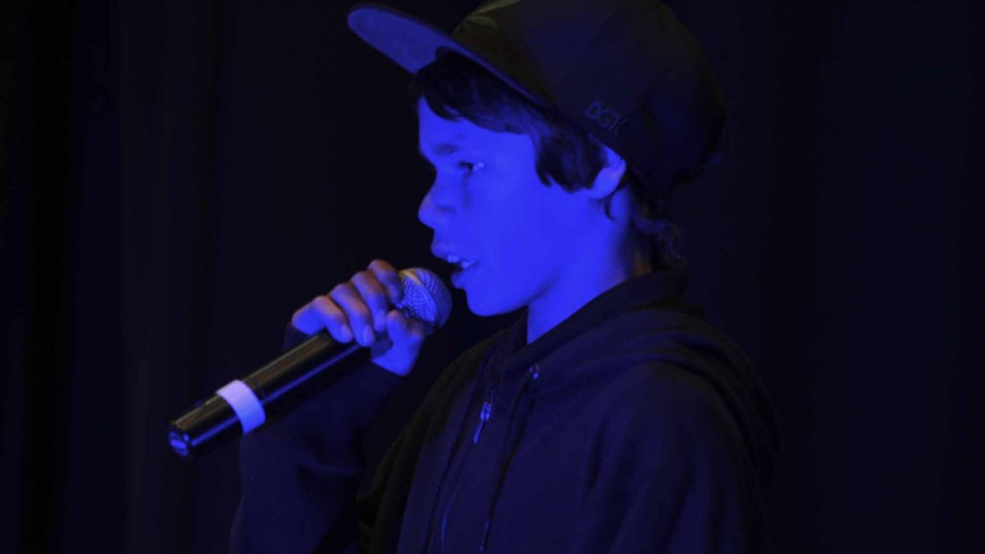 Young boy with a hat on singing into a microphone