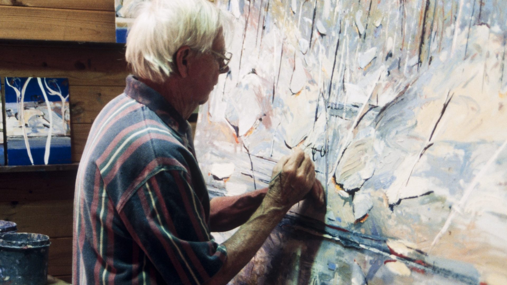 Person with short white hair paints a large abstract landscape painting