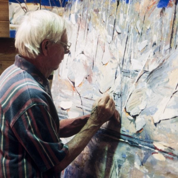 Person with short white hair paints a large abstract landscape painting