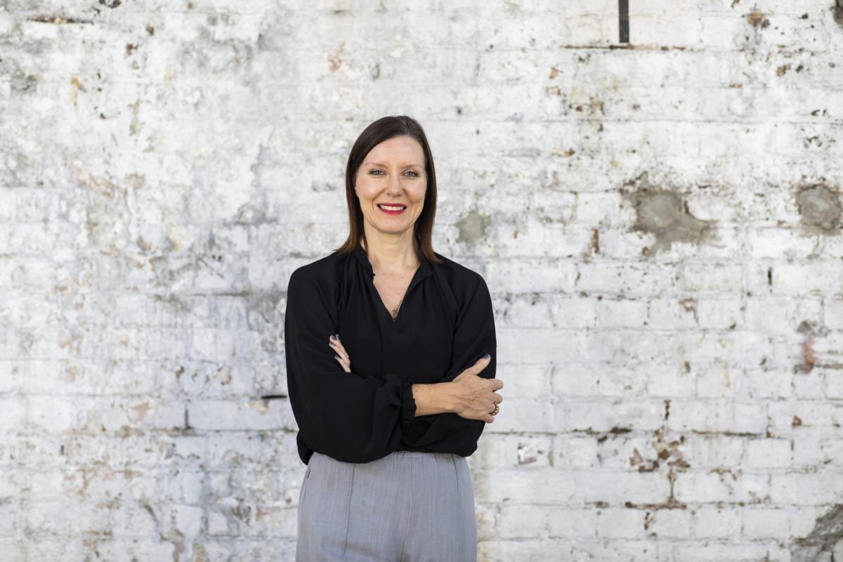 A person with short dark hair, crossing their arms and smiling at the camera