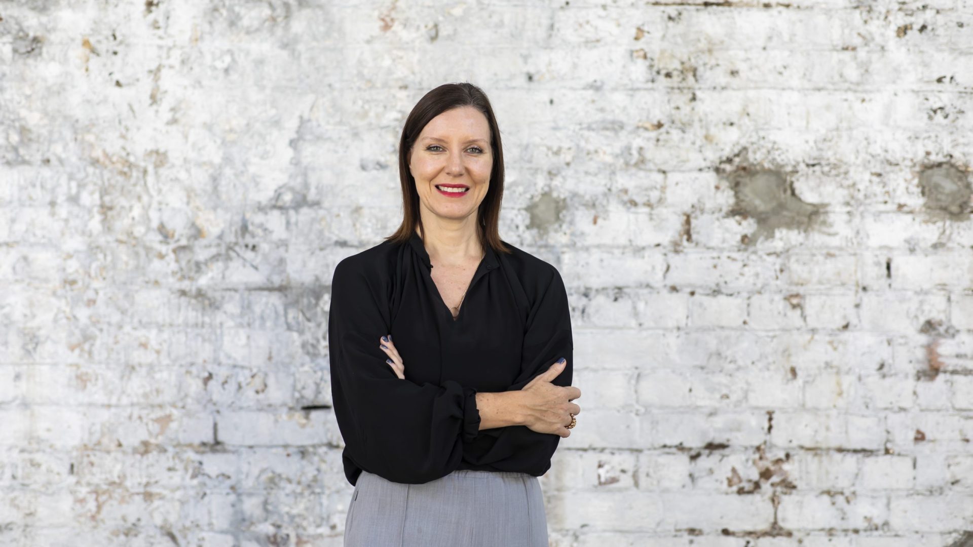 A person with short dark hair, crossing their arms and smiling at the camera
