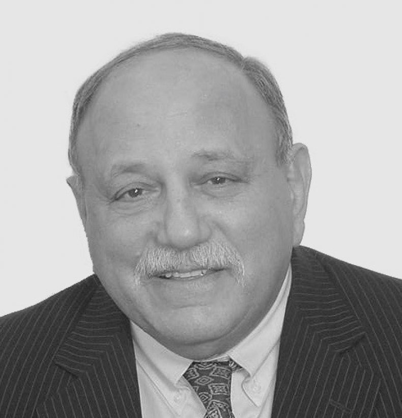 A person with short hair and a moustache, wearing a suit and tie