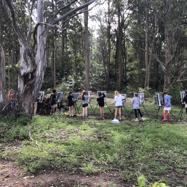 12 children standing at easels, drawing black and white pictures of trees in a landscape