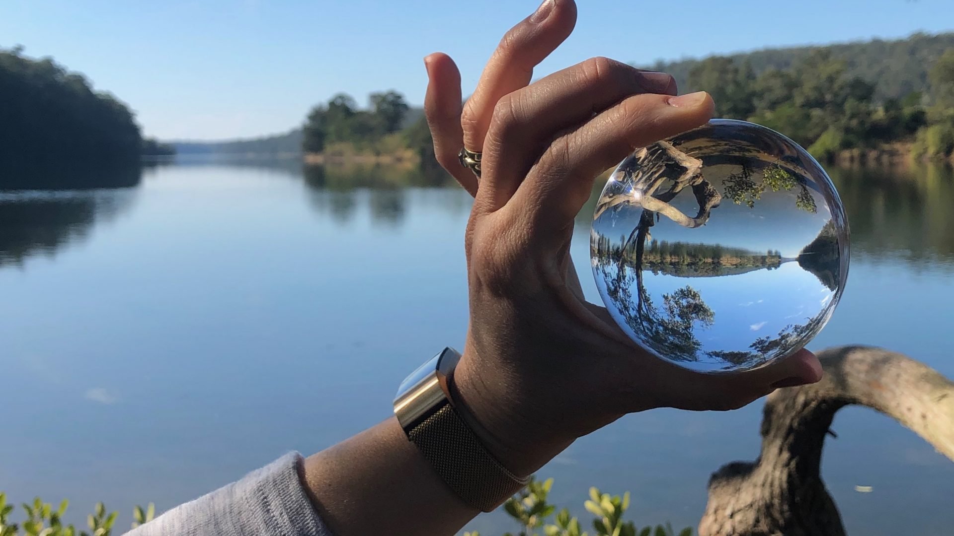 A hand holding a glass ball in front of a river landscape