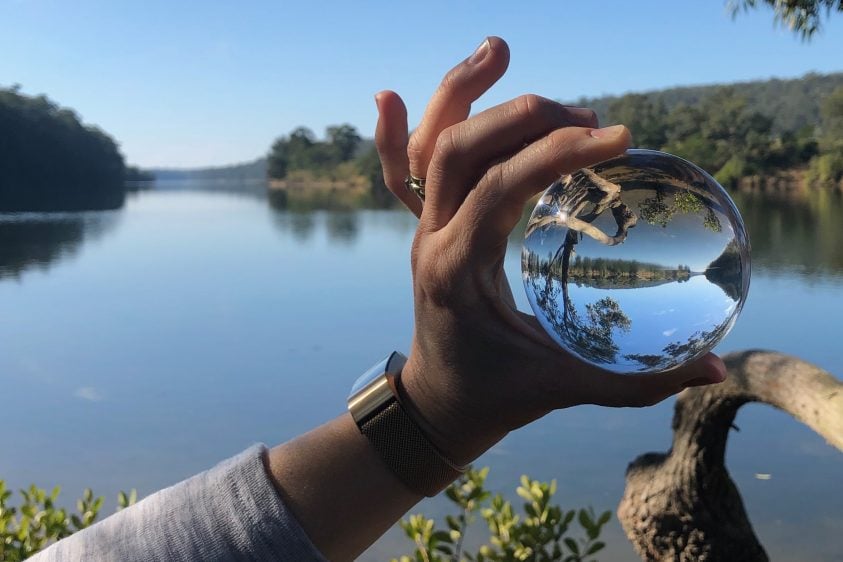 A hand holding a glass ball in front of a river landscape