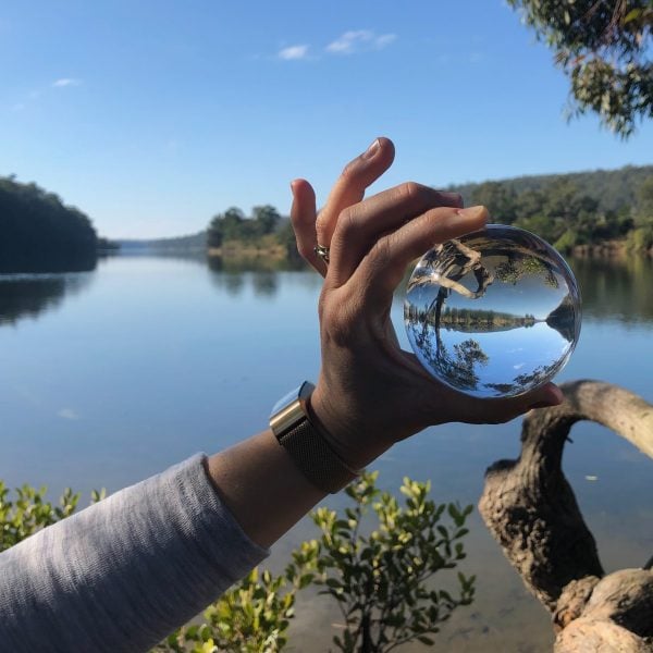 A hand holding a glass ball in front of a river landscape