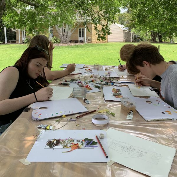 4 people sitting at a table drawing, a stone building is in the background