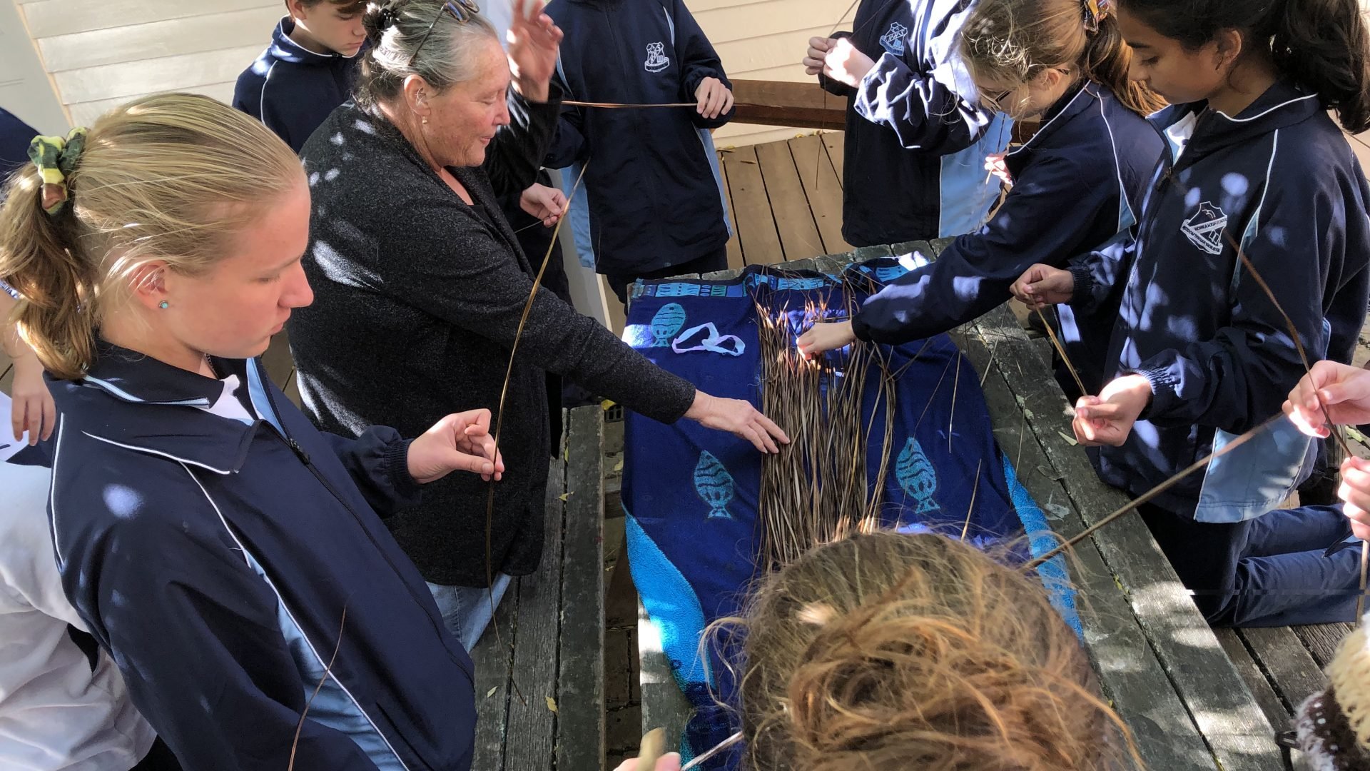 9 school children in blue uniforms standing around a table, they're all holding grasses