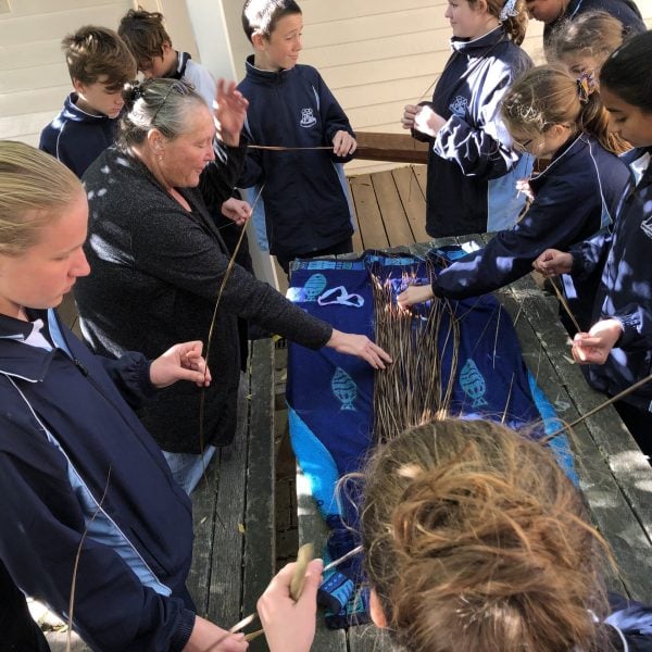 9 school children in blue uniforms standing around a table, they're all holding grasses