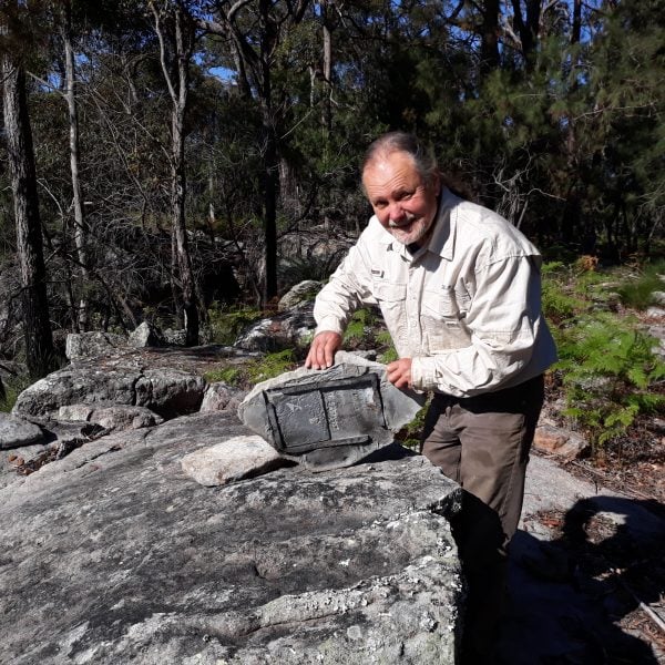 A person holding up a concrete slab that is resting on a large rock
