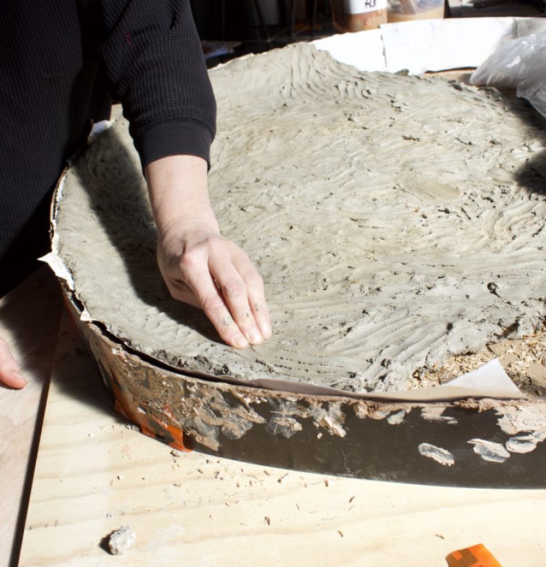 A person's hand pushing into clay in a large tray