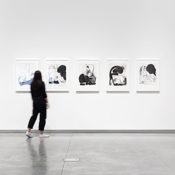 Person in a white art gallery space looking at abstract black and white drawings