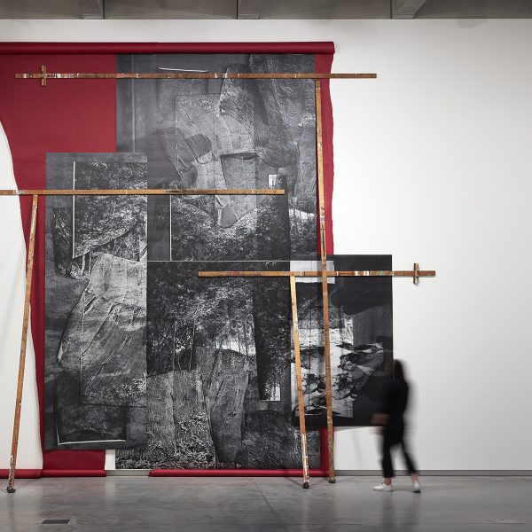 A person looking at an abstract black, white and red artwork on a wall in a large white gallery space