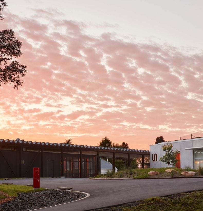 A concrete building in a landscape with a tall gumtree in the foreground.