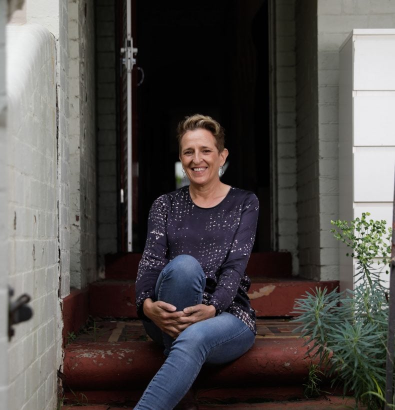 A person with short brown hair sitting on a step, smiling