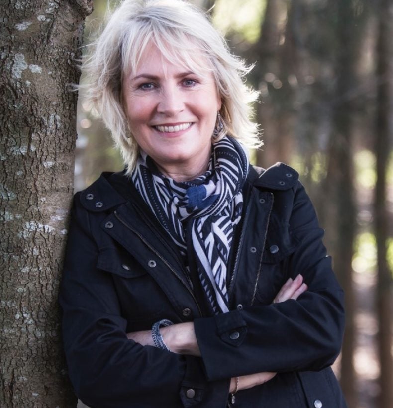 Person with short blonde hair, arms crossed smiling