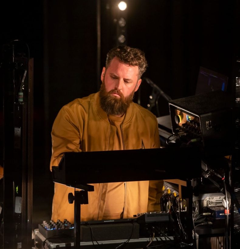 A person with a beard standing at a mixing desk