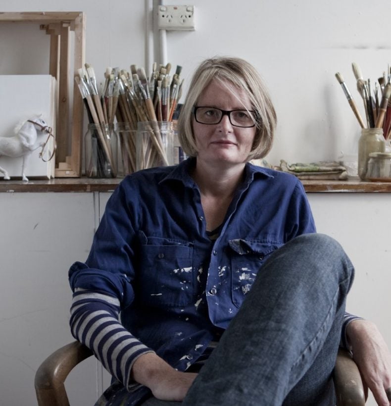 A person sitting on a chair with a shelf behind them with paintbrushes in jars