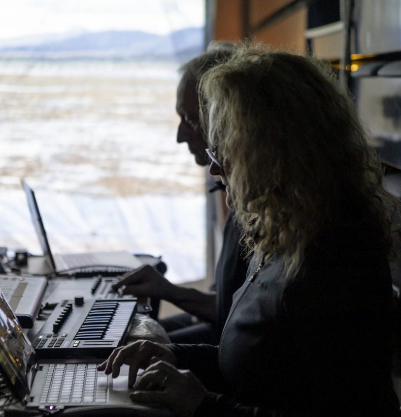 Two people sitting at a desk with laptops and a keyboard