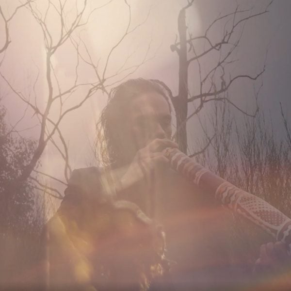 Misty photo of a person playing a didgeridoo in a burnt tree landscape