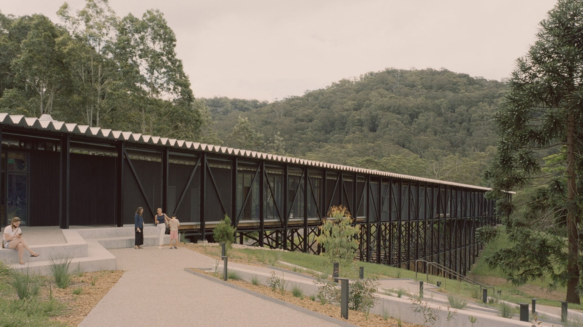 Black building extending over a gully, mountains in the background