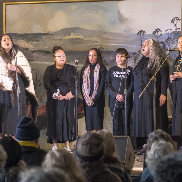 6 people standing on a stage and singing into microphones