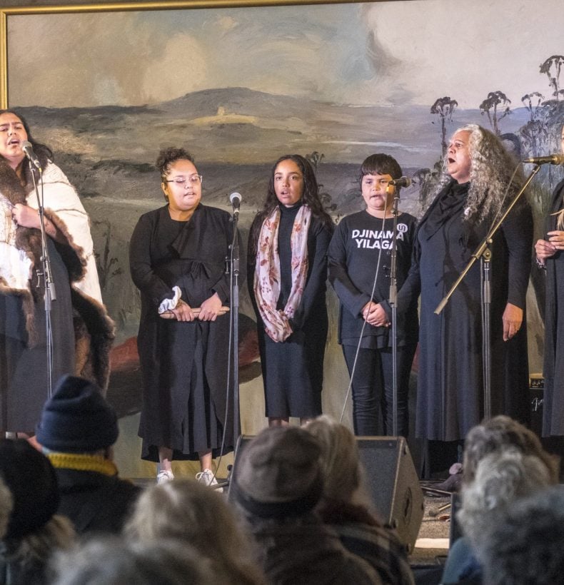 6 people standing on a stage and singing into microphones