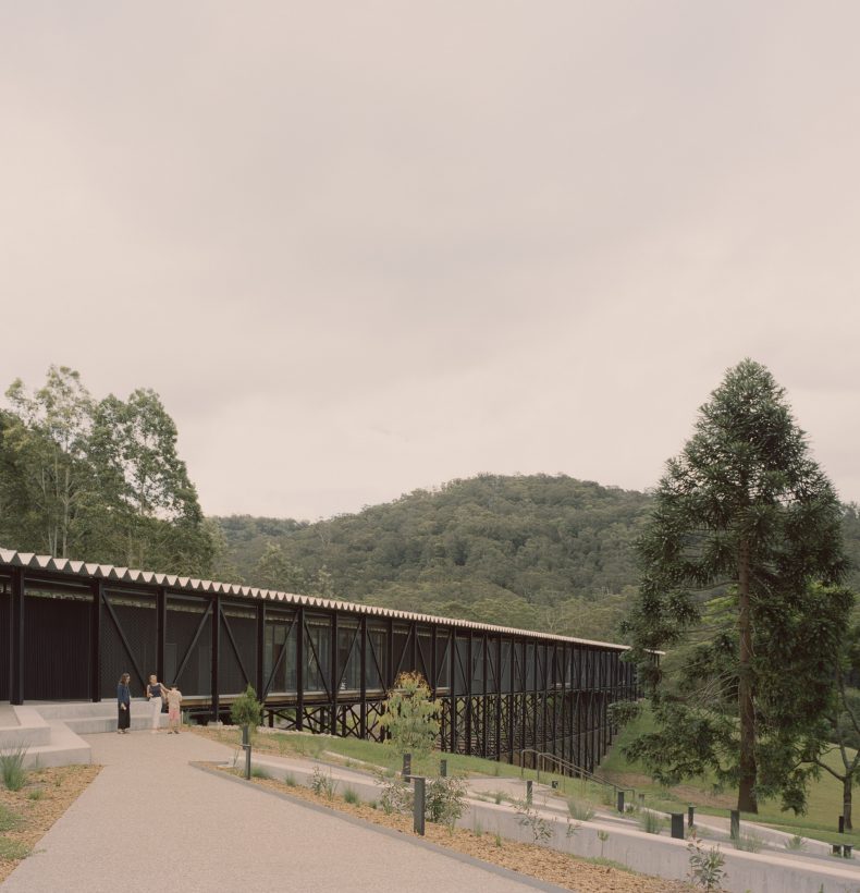 Black building extending over a gully, mountains in the background