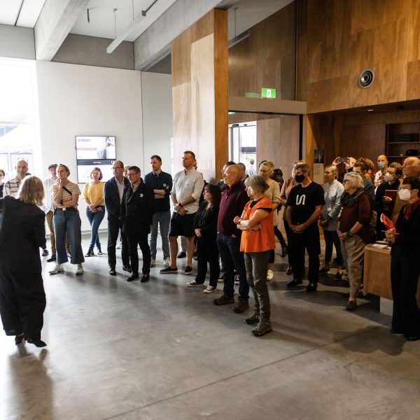 Group of people in a room being directed by someone pointing to a wall