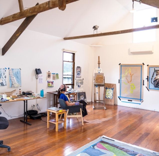 Artist Tai Snaith sits in an armchai in the Barn Studio reviewing her work on the walls