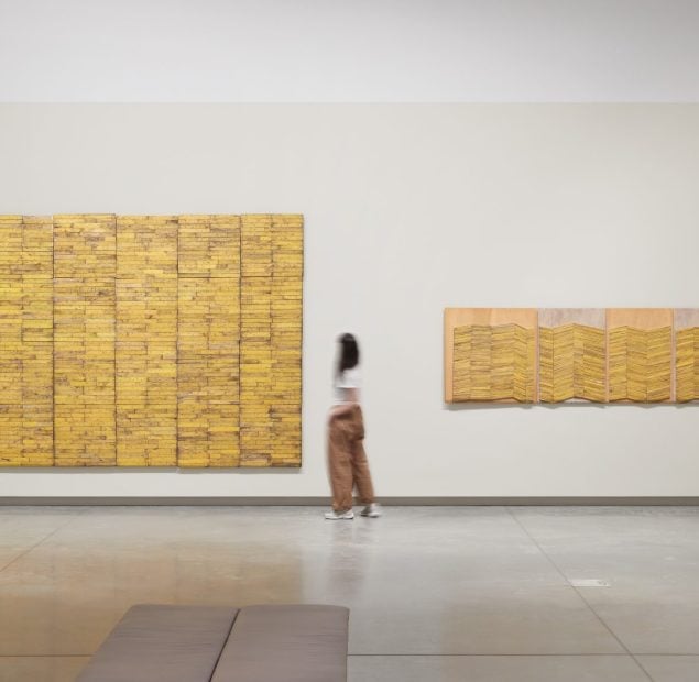 Human walking amongst large yellow artworks on the wall of an open space.