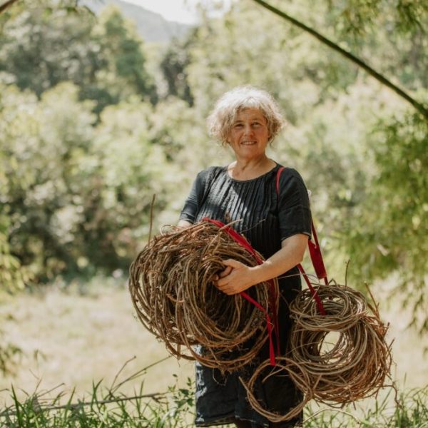 Woman with weaving shroud in hand, stands outside.