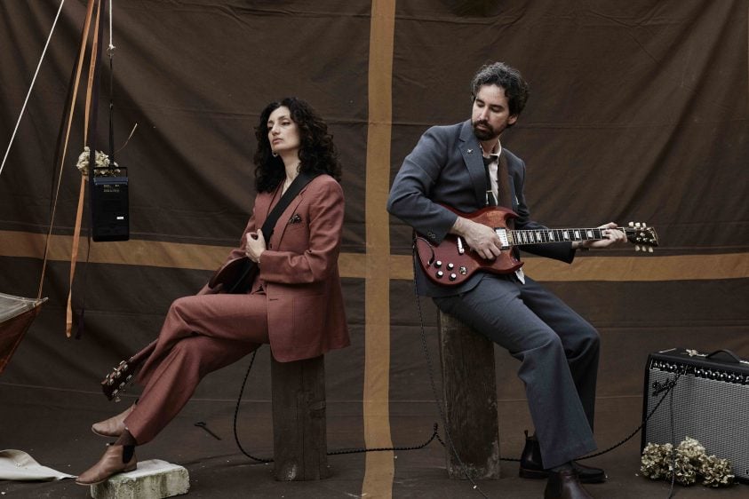 Two people sit back to back one, holding a guitar.