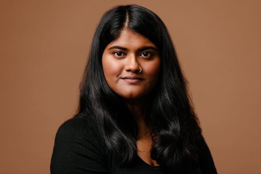 Woman with long hair looks at the camera within a studio, with a brown background.