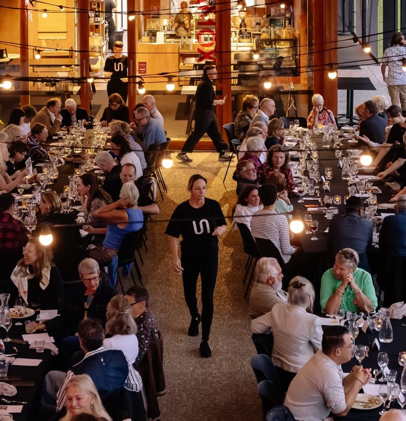 An above ground view many people at dining tables in an undercroft area.