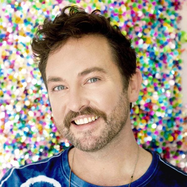 Man smiles at camera with glitter on the wall behind him.