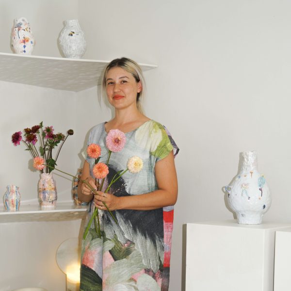 Woman wearing a colourful dress holds a flower in hands.