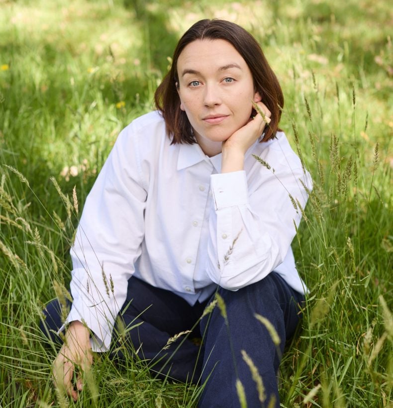 Person rests on hand whilst sitting in the tall grass outside.