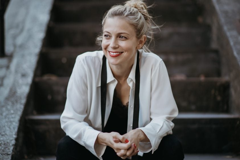 Woman smiles whilst sitting on outdoor steps.