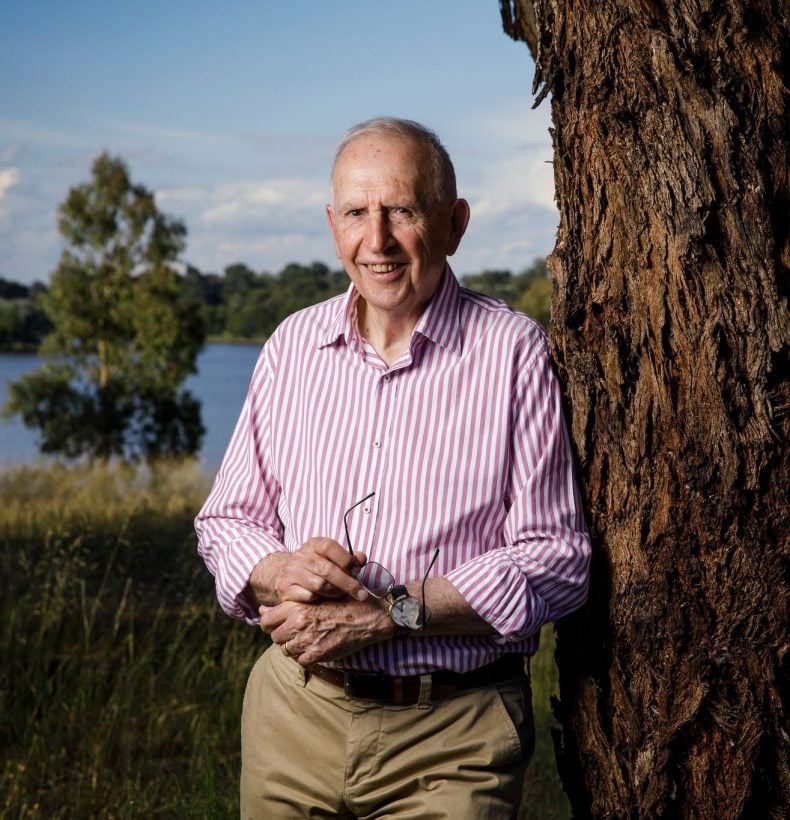 Man smiles as he leans on a tree.