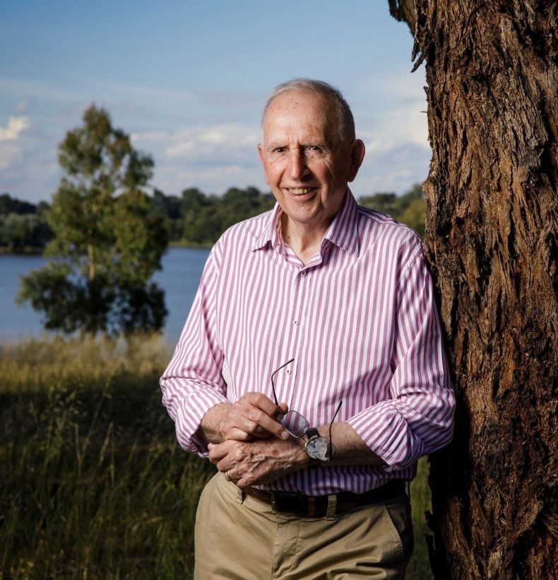 Man leans on a tree near a lake.