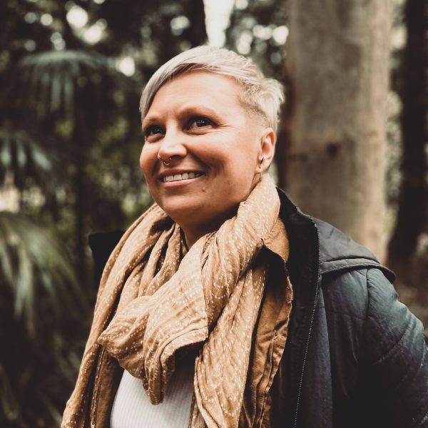 Woman with short hair stands in the bush, looking upwards.