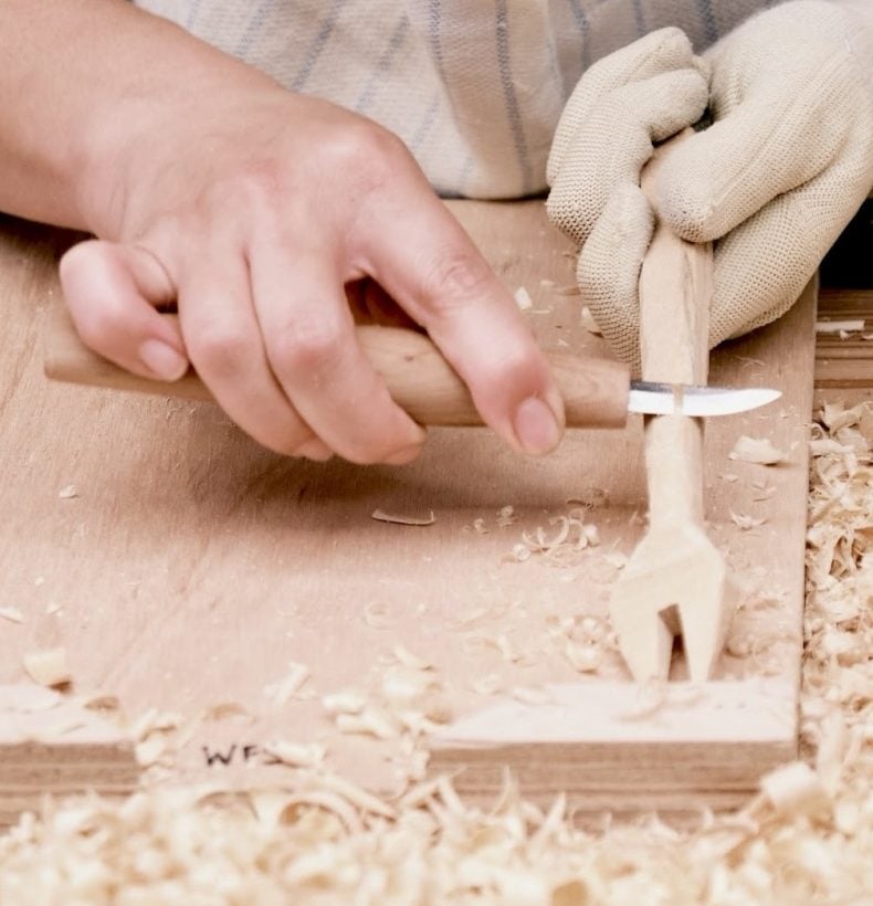 Close-up view of hands work on carving a fork on a work bench.