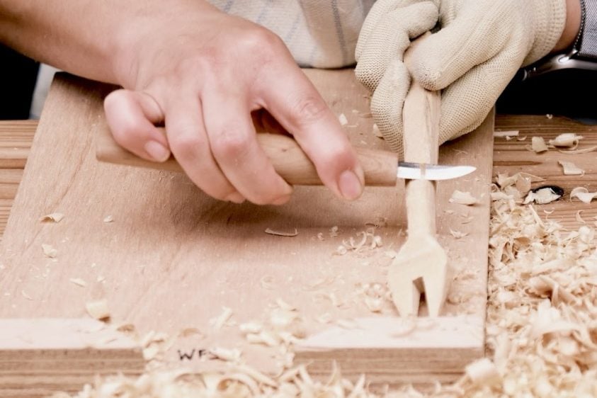 Close-up view of hands work on carving a fork on a work bench.