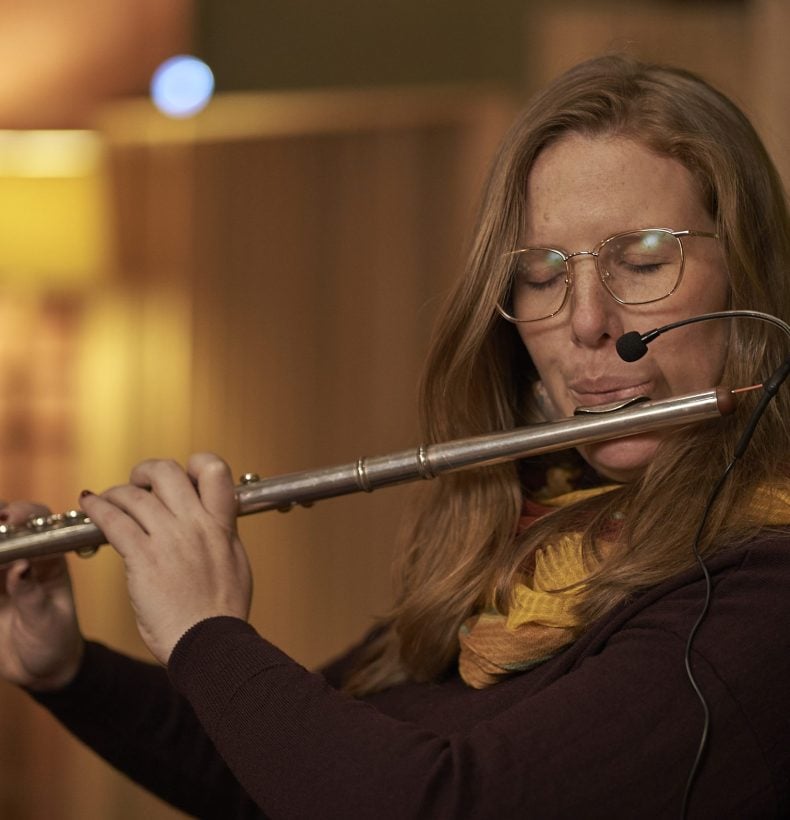 Woman playing the flute in a warmly lit space.