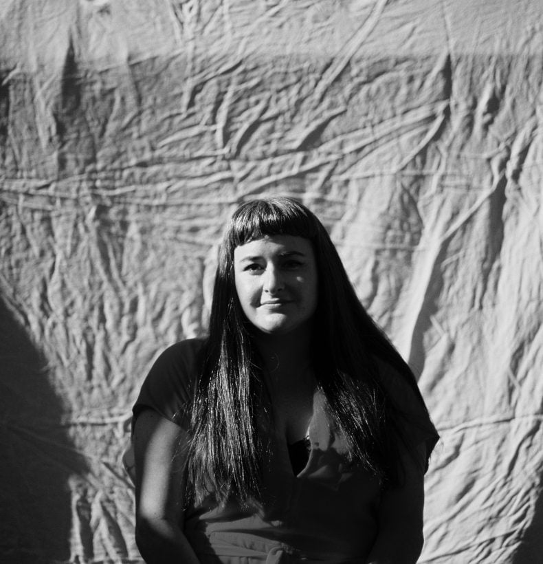 Woman with a fringe standing infront of sheet in a black and white portrait.
